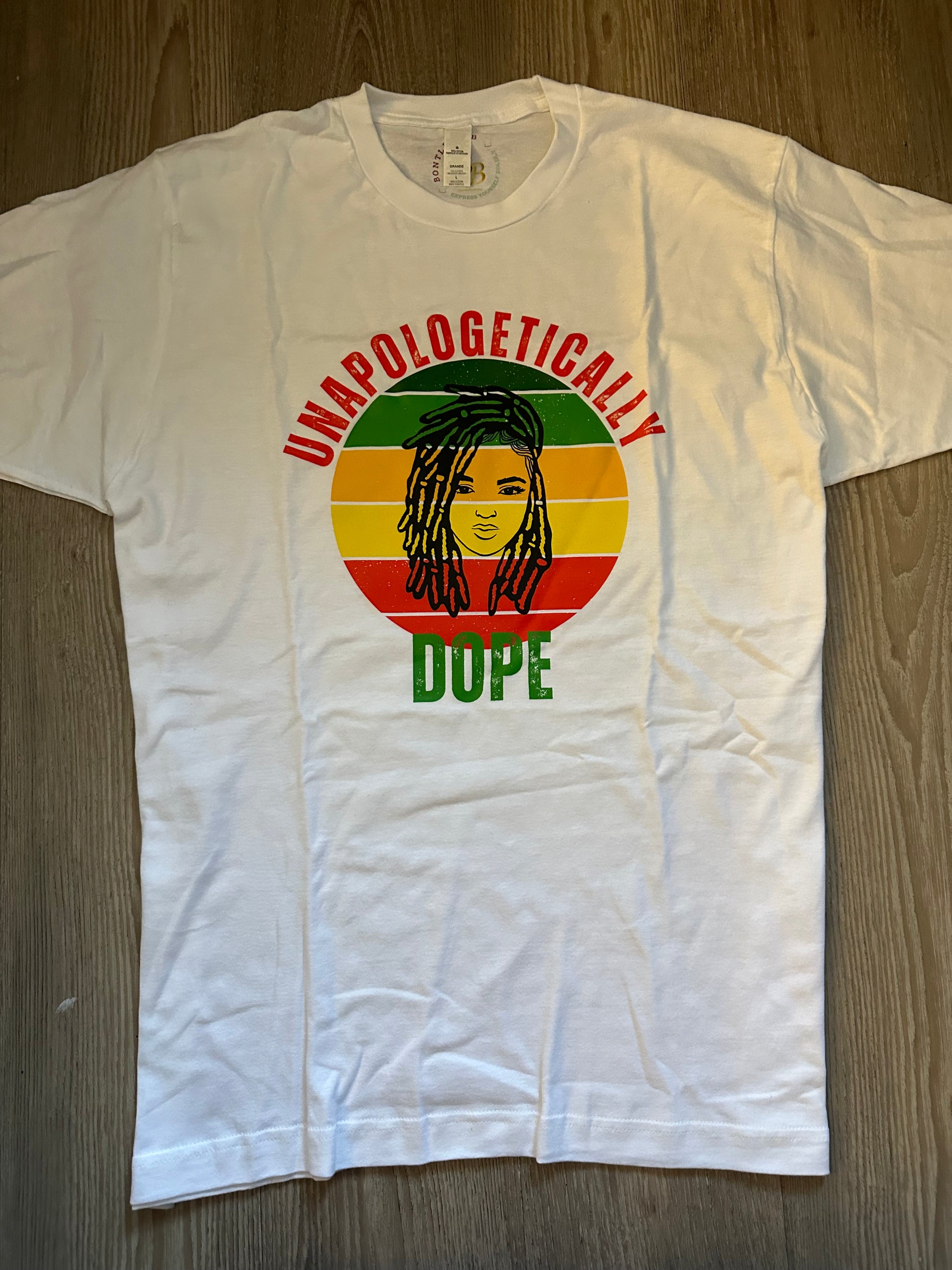 Unapologetically in Red text Dope in green text with green, orange, yellow, red retro circle with dreadlocks lady on top on a white shirt. Melanin Apparel.