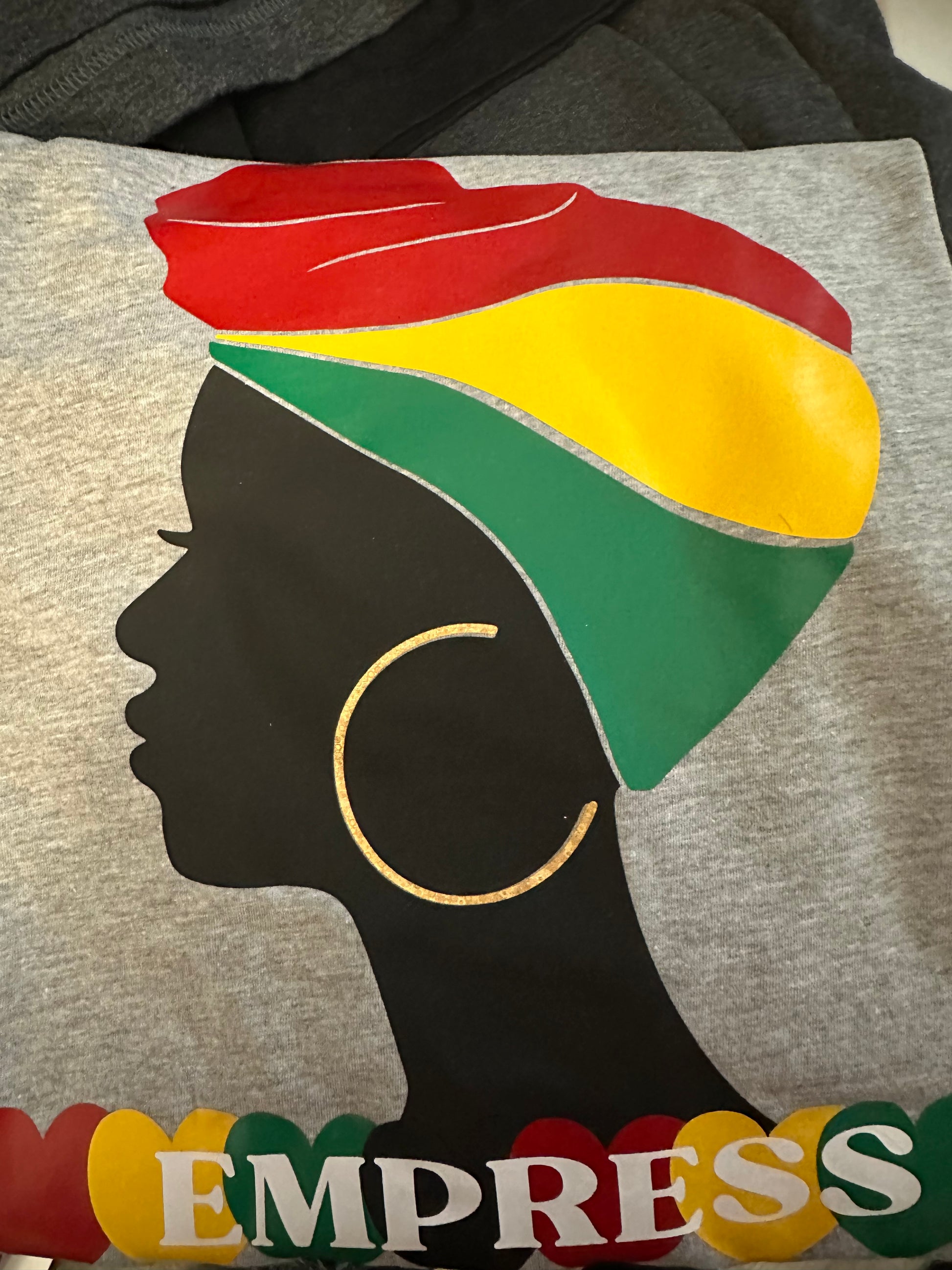 Heather Grey V-neck shirt with black woman silhouette with red, yellow and green headwrap with gold large earrings. Below the silhouette hearts yellow, red, green and black repeatedly with word Empress in white. Melanin apparel.