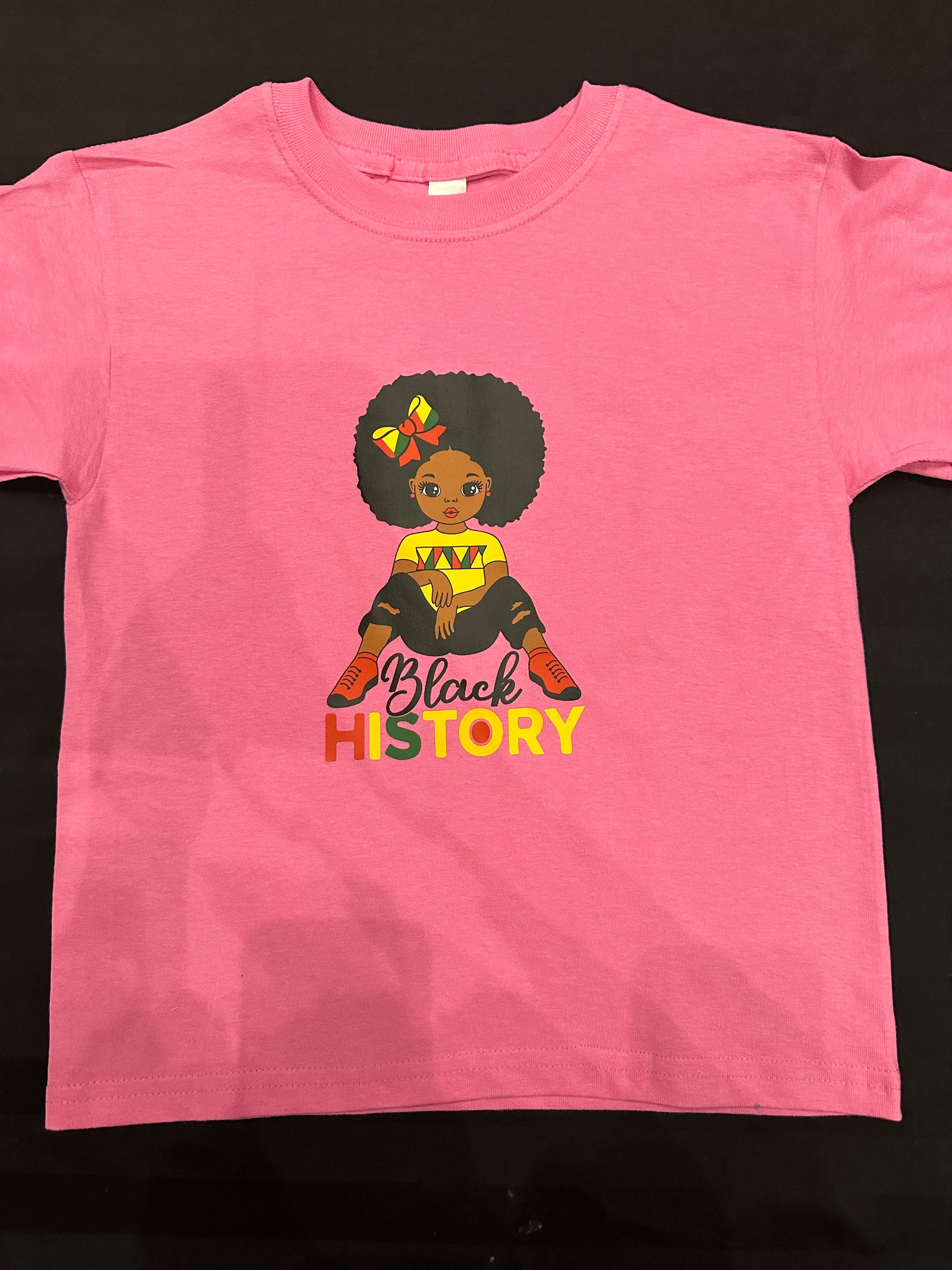 Pink shirt with black girl with Afro with red yellow and green bow in her hair wearing a yellow shirt with red and green markings on the chest and black ripped jeans and red shoes with black in black cursive text and History is red, yellow and green block text. Melanin Apparel.