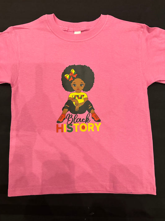 Pink shirt with black girl with Afro with red yellow and green bow in her hair wearing a yellow shirt with red and green markings on the chest and black ripped jeans and red shoes with black in black cursive text and History is red, yellow and green block text. Melanin Apparel.