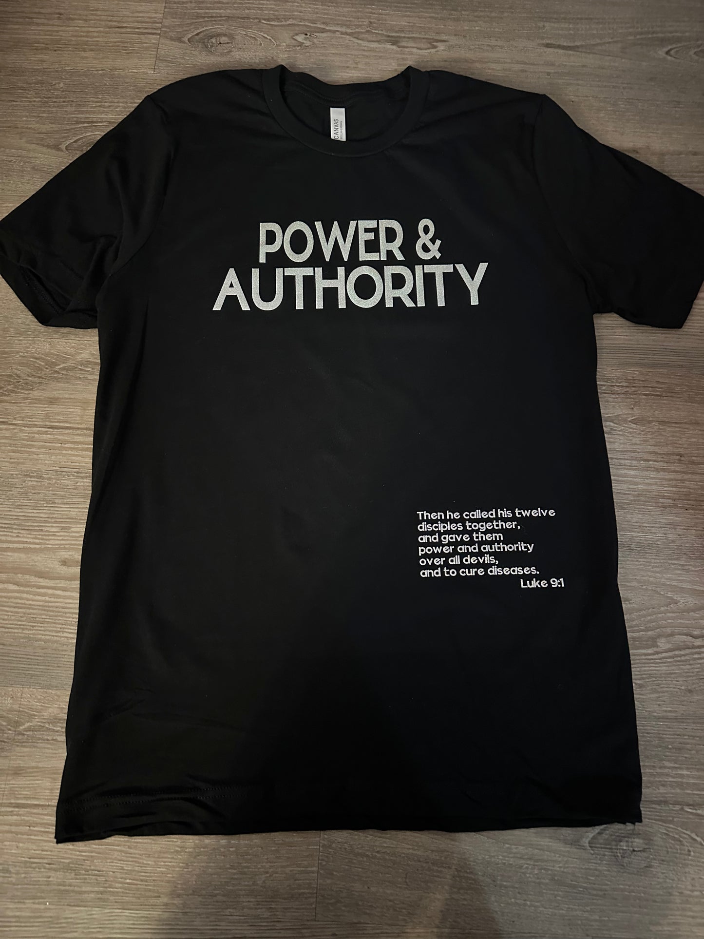 Black shirt with silver glitter text Power & Authority in the middle with scripture Luke 9:1 on the left. Christian apparel.