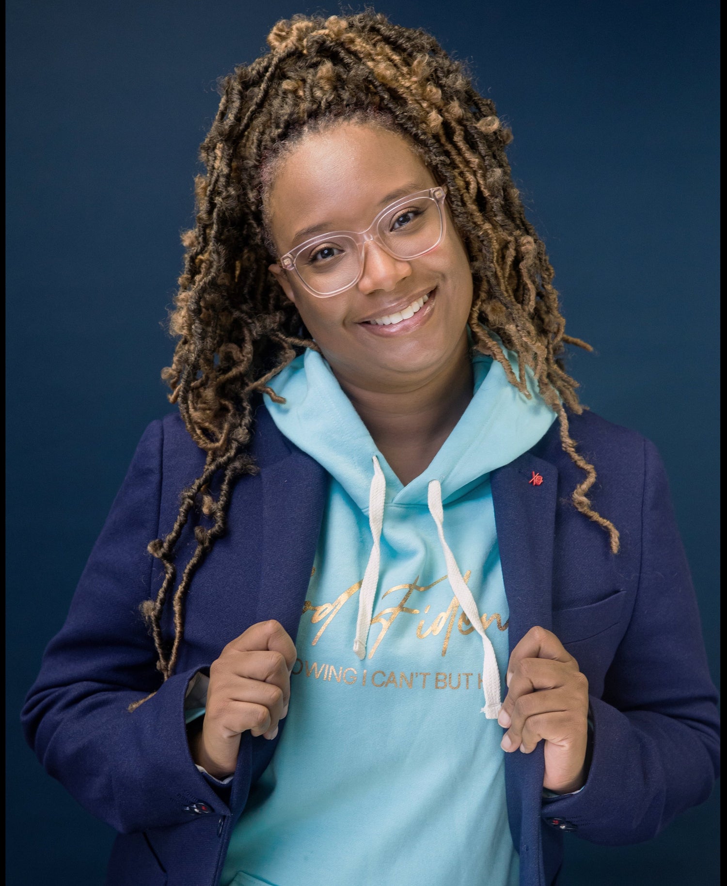 Person wearing a blue jacket over a light blue hoodie with Godfidence in gold on a dark background